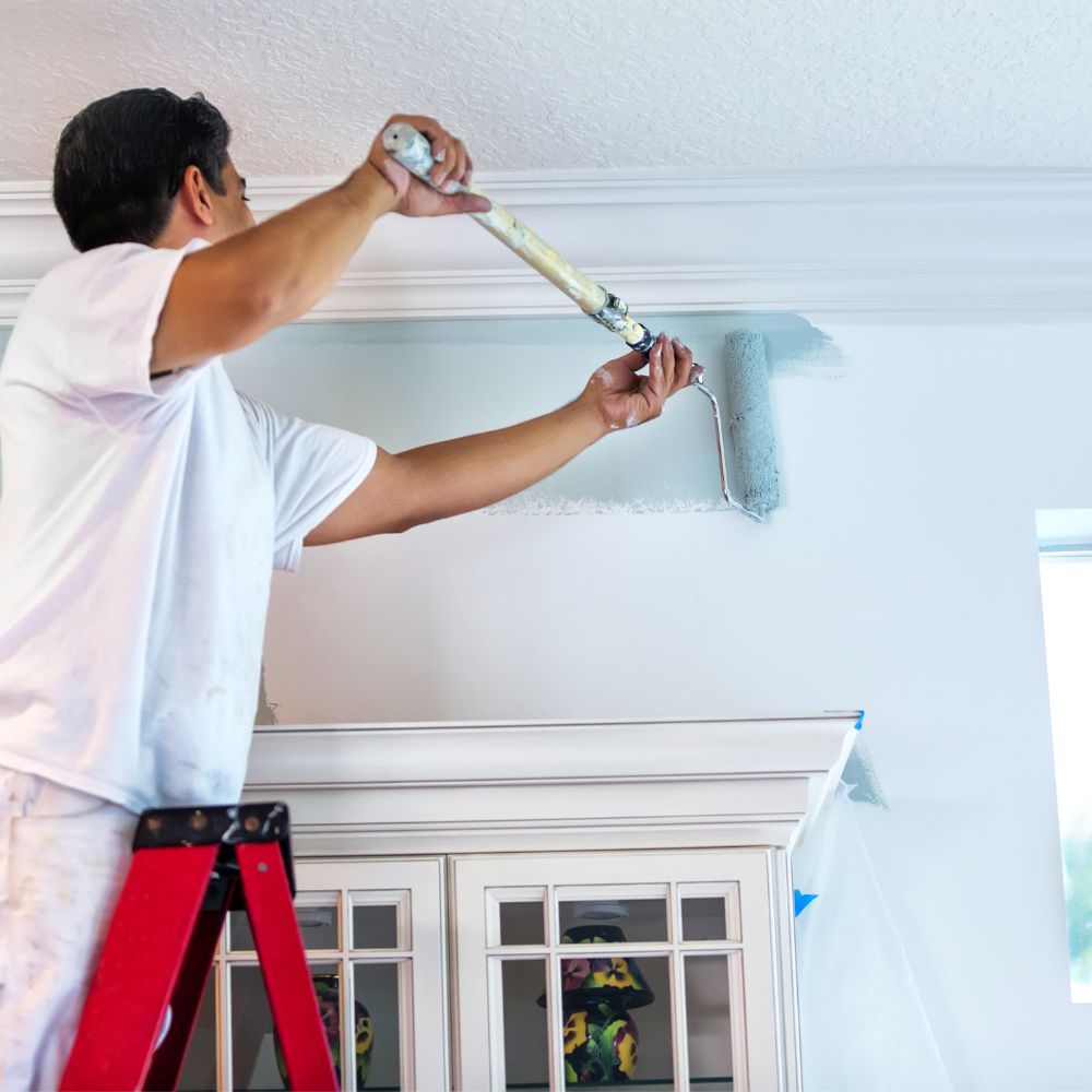 Painter rolling a light-blue interior wall near crown moulding using Diamond Brite latex paint.