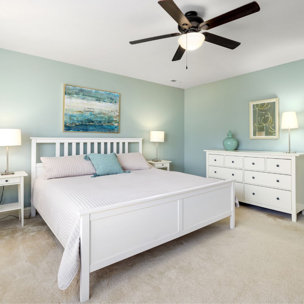 Calm bedroom with soft blue-green painted walls, white bed frame, and dressers.