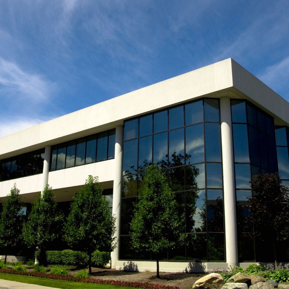 Modern office building with white exterior paint and black window trim, landscaped trees.